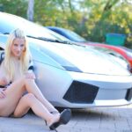 Kinky blonde MILF Haley shows her huge boobs and poses in front of a car